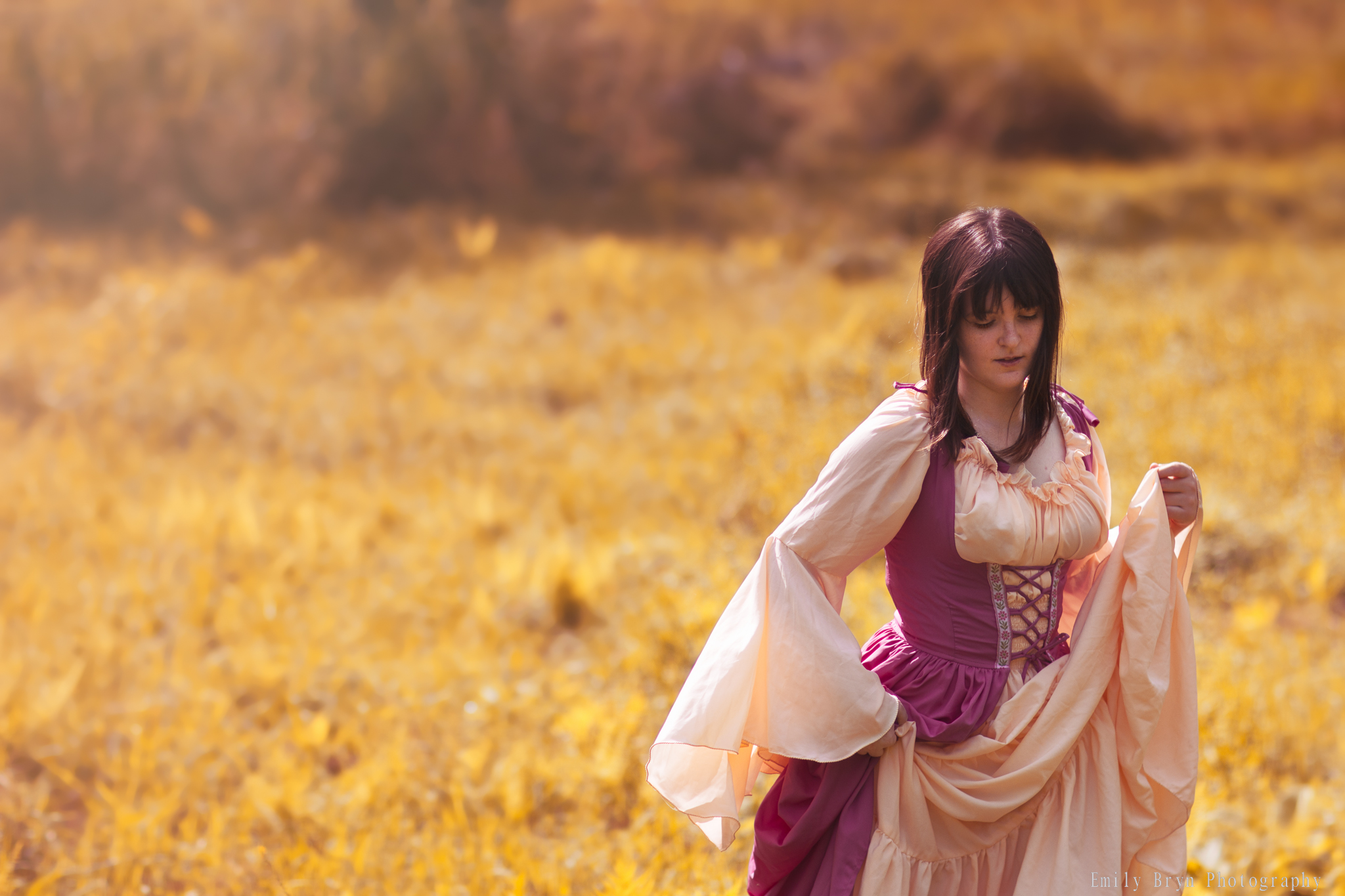 Woman walking through a field, wearing a renaissance dress.