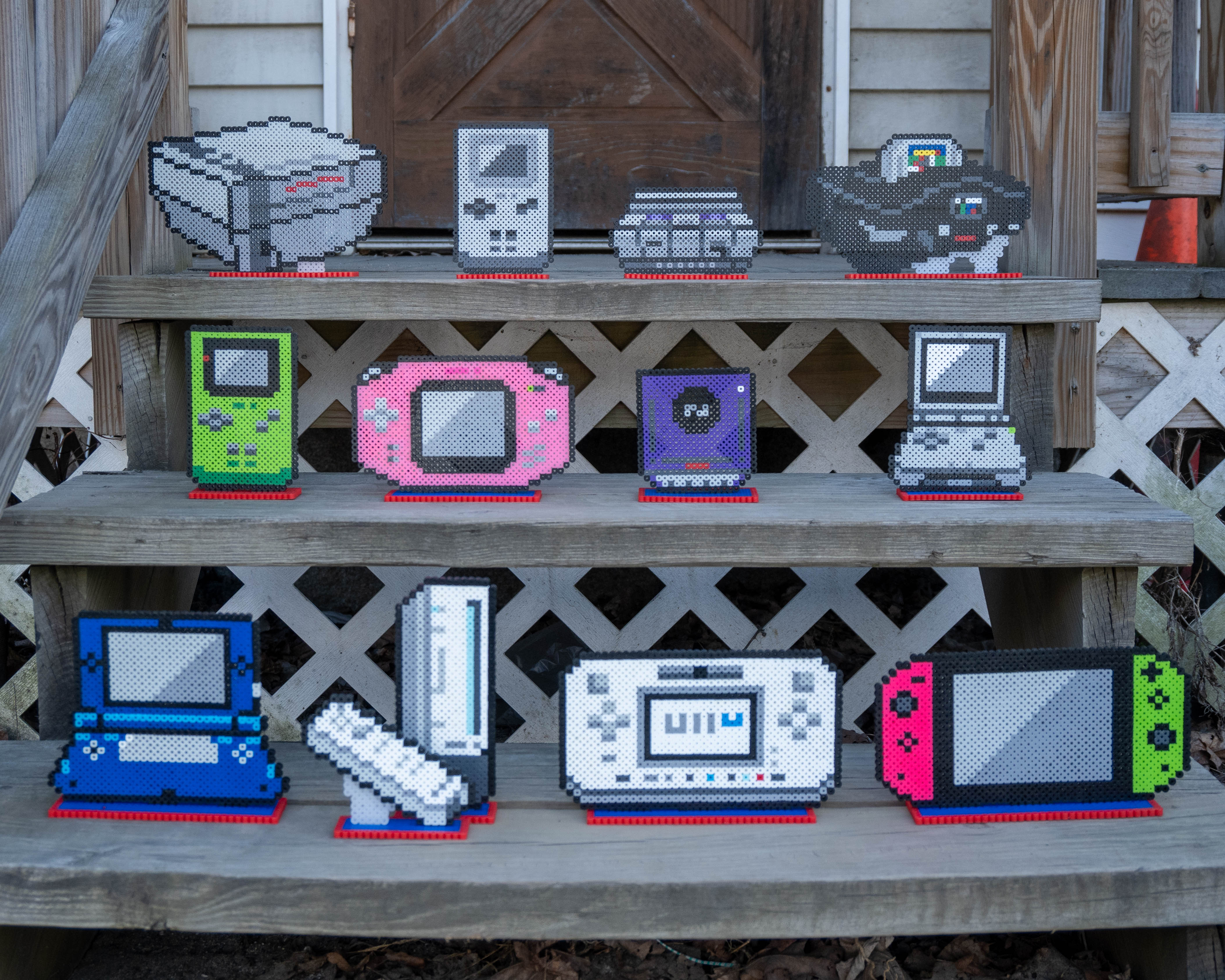 All Nintendo Consoles made out of fuse beads, arranged on wooden steps.