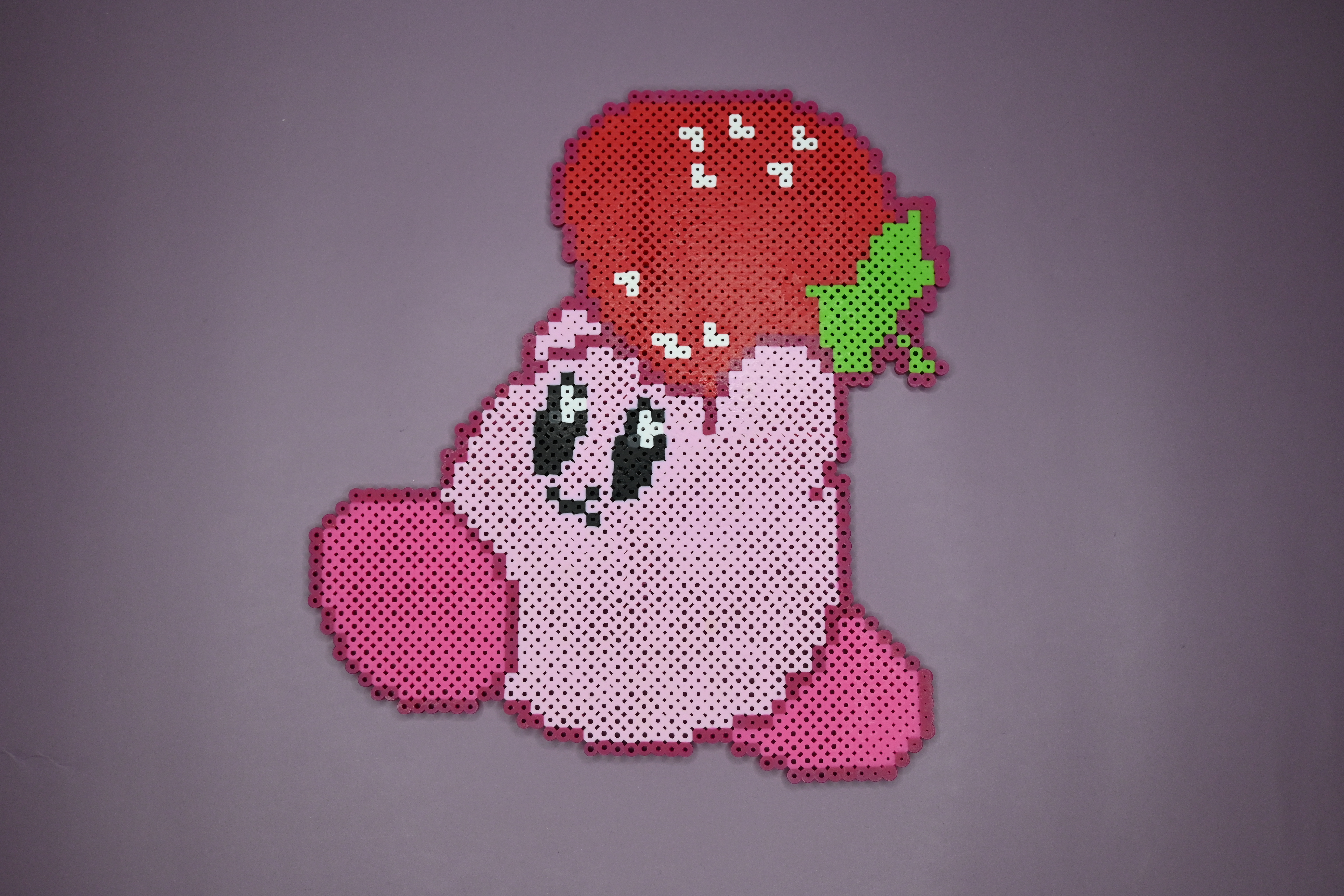 Pink Kirby running while carrying with a strawberry made out of Perler brand fuse beads.