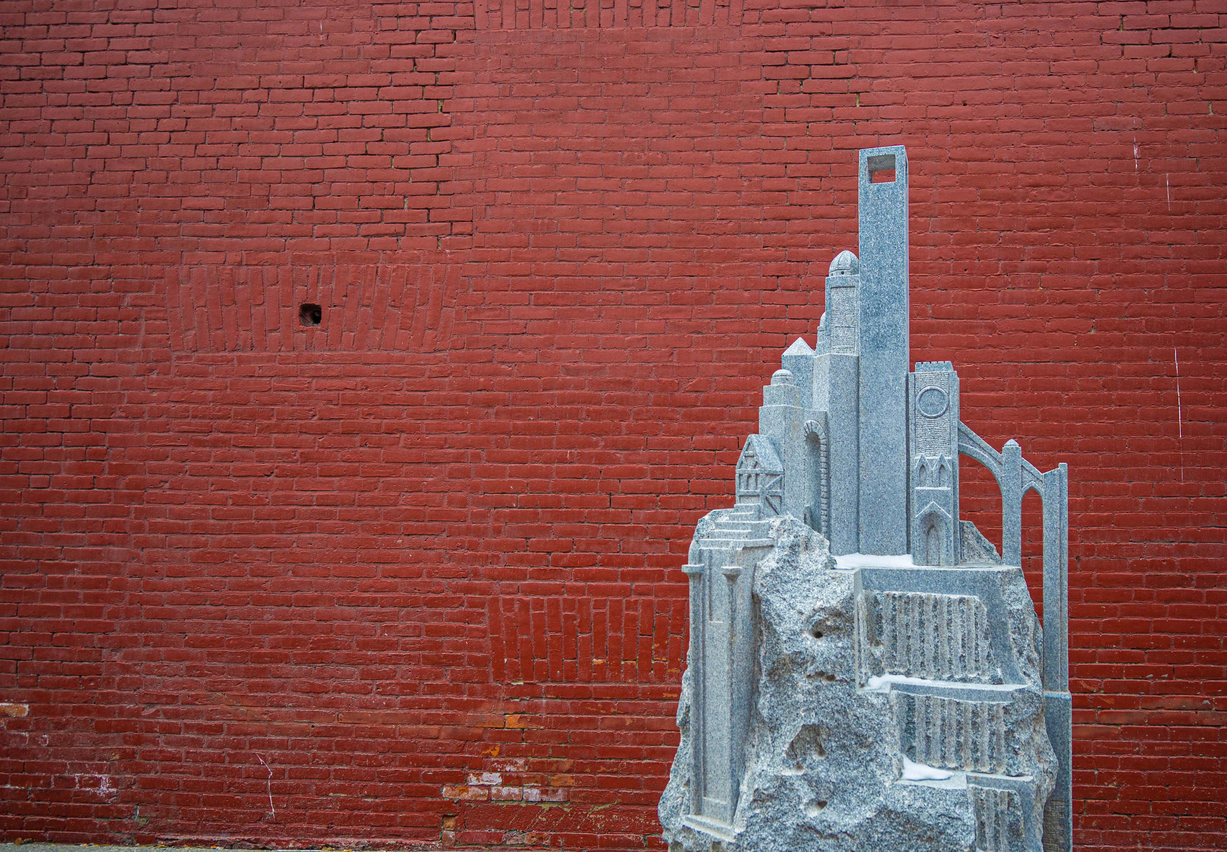 A light grey granite statue against a red brick wall.