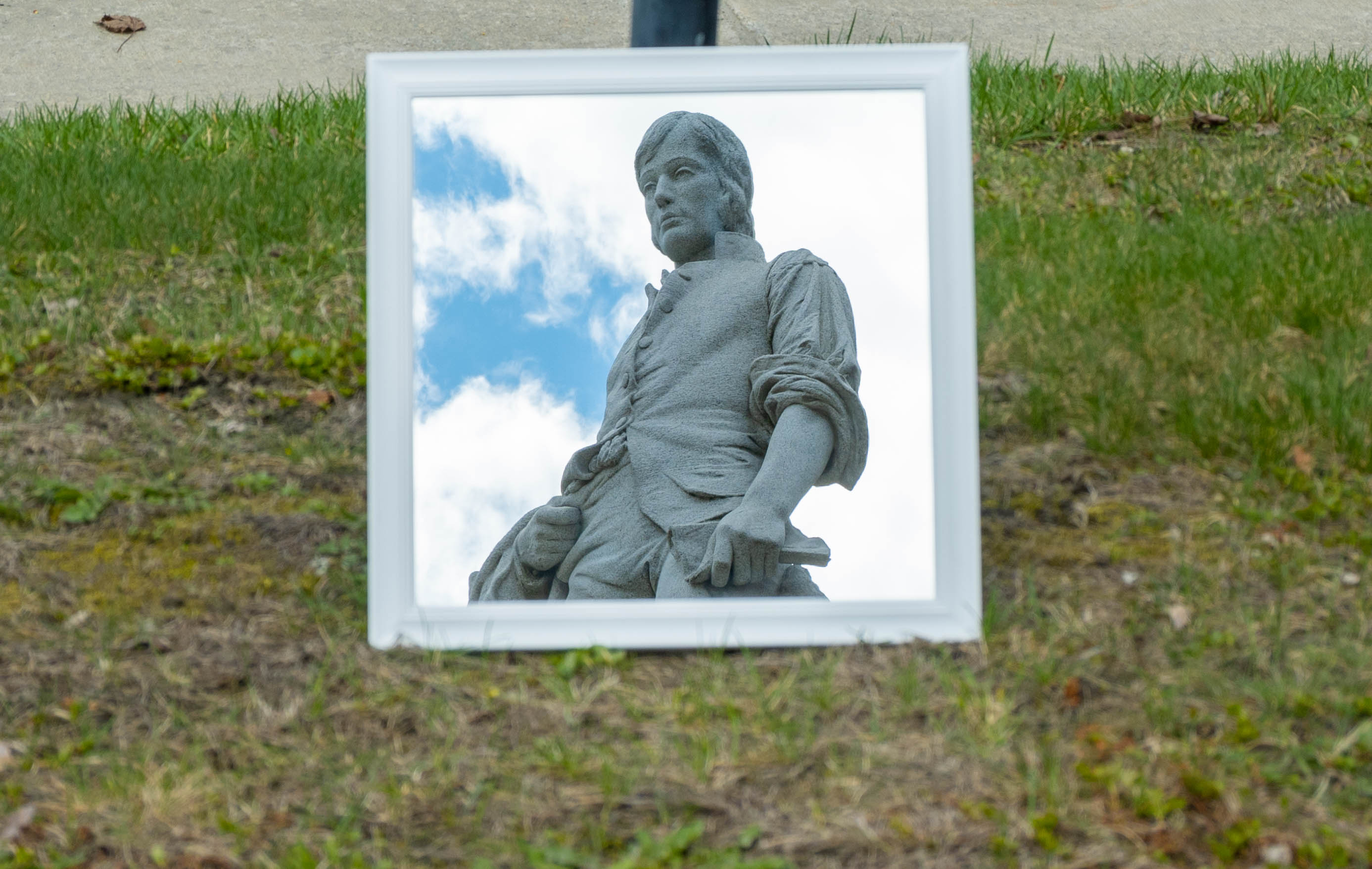 Reflection of a granite statue in a mirror on the grassy ground.