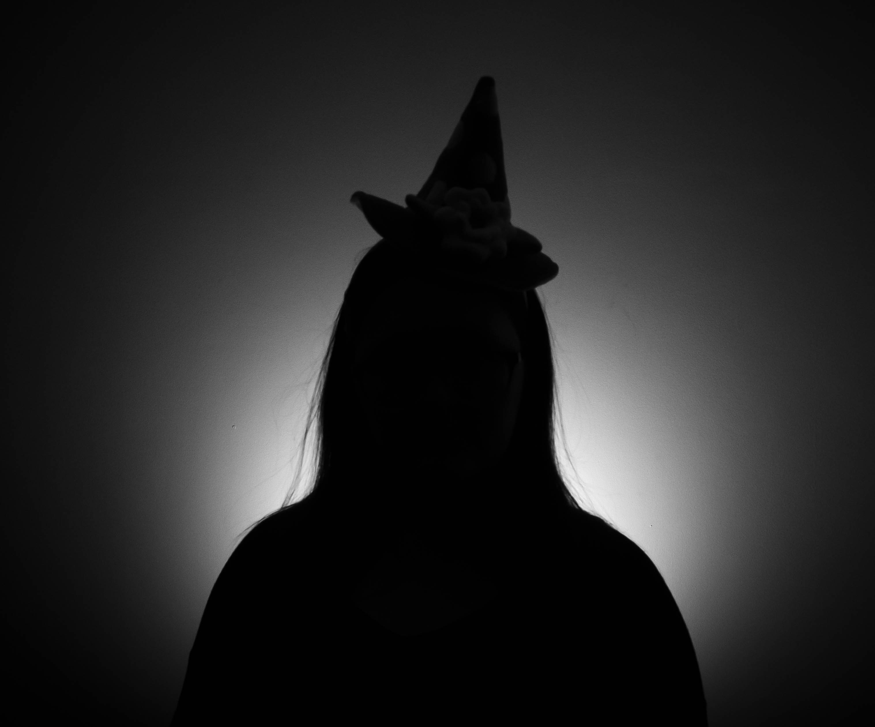 Shadow with a witch hat against a white light background.